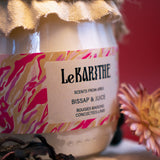 Bougie parfumée aux senteurs de bissap (boisson à base d'infusion aux fleurs d'hibiscus), aux ingrédients sains et simples, sur fond rouge.